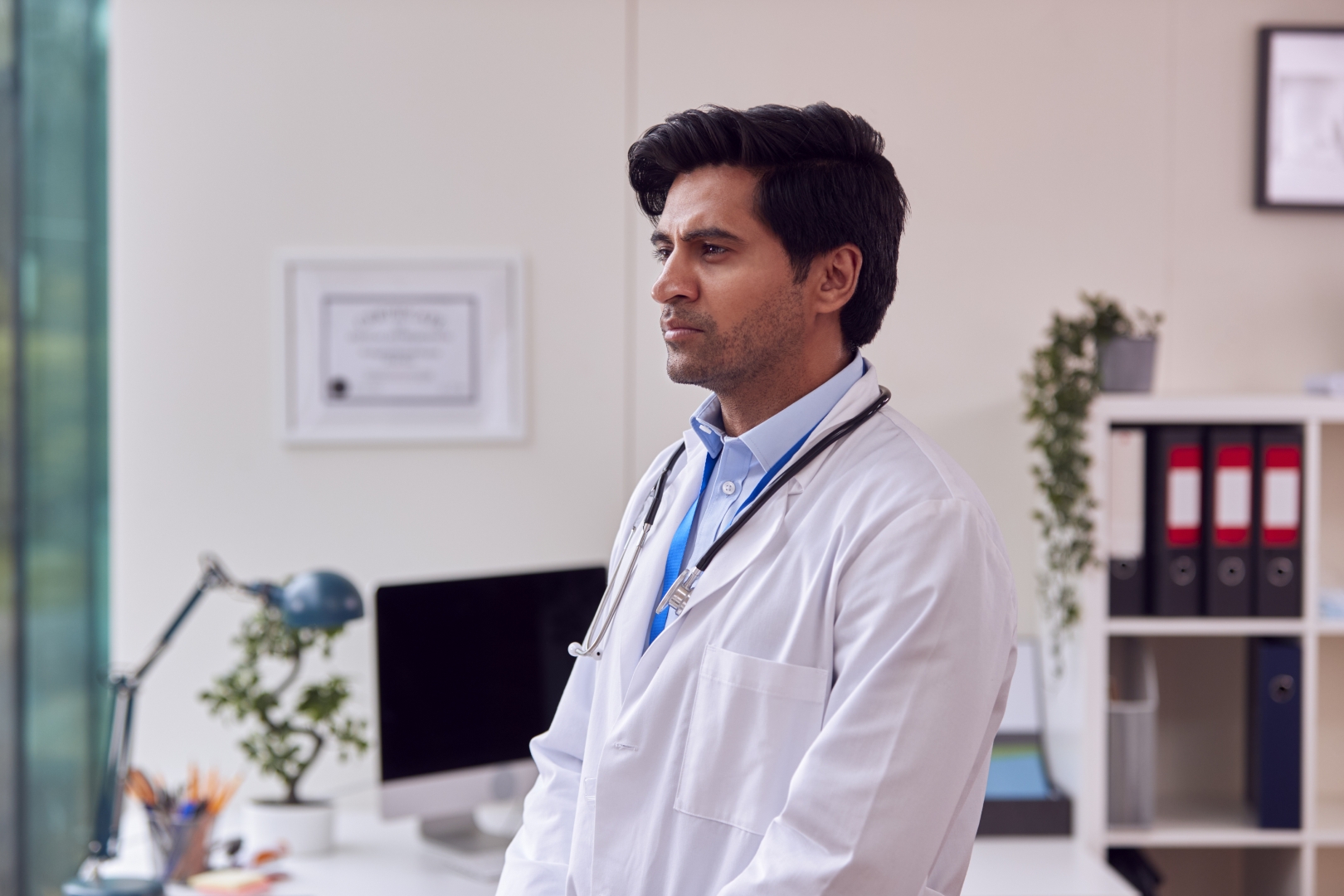 Un médecin, en blouse blanche avec stéthoscope dans un bureau médical, pense à son hypothèque pour professionnels de la santé