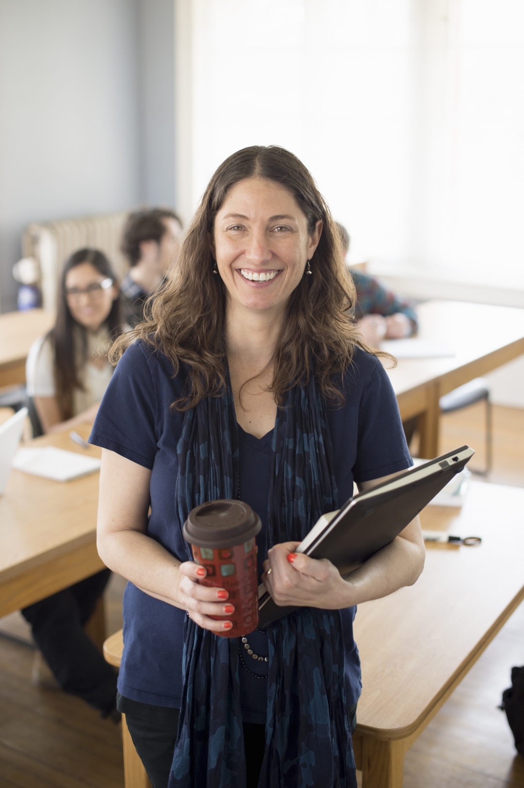 Femme enseignante souriante tenant un café et des cahiers en salle de classe